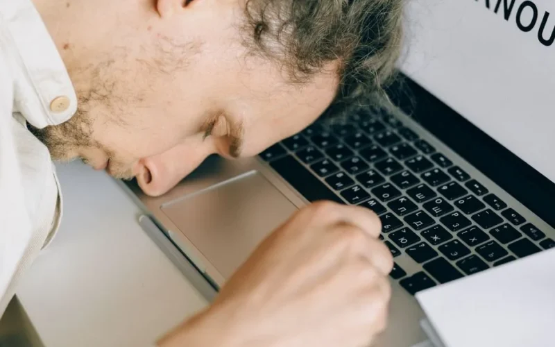 Exhausted employee resting head on laptop keyboard due to burnout and stress.