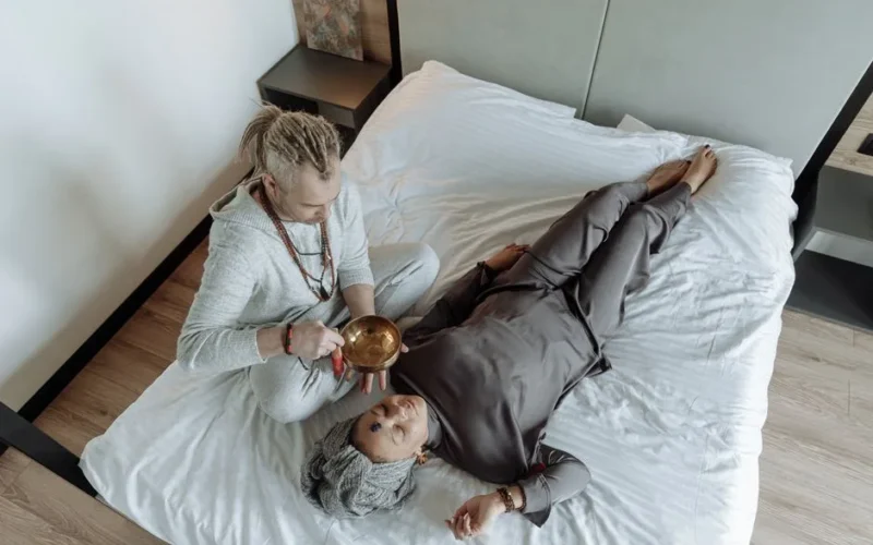 A man and woman involved in a spiritual healing session with a singing bowl on a bed.
