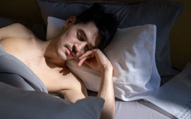 A man peacefully sleeping in a sunlit bedroom with natural light streaming in.