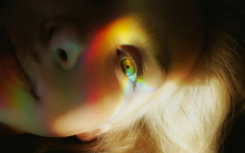 Close-up portrait of a woman with rainbow light reflections creating a surreal effect.