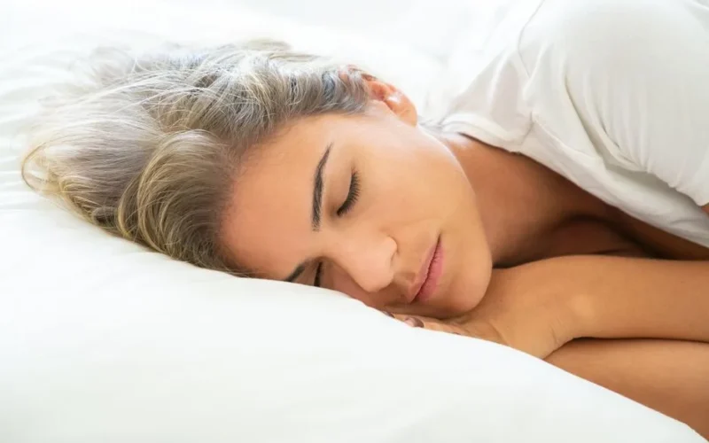 A relaxed woman with blond hair sleeping peacefully on a white pillow indoors.