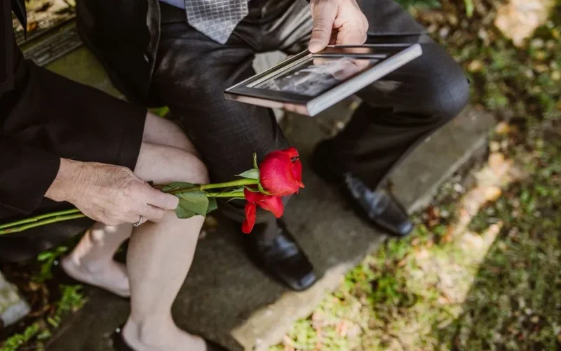 A grieving couple sitting with a red rose and a picture frame in their hands.