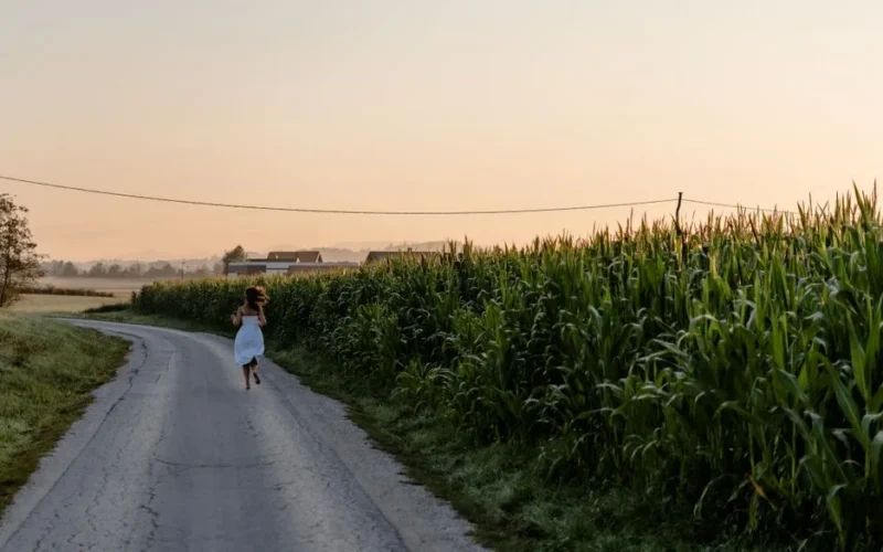 A woman in a white dress runs barefoot on a countryside road during sunrise.