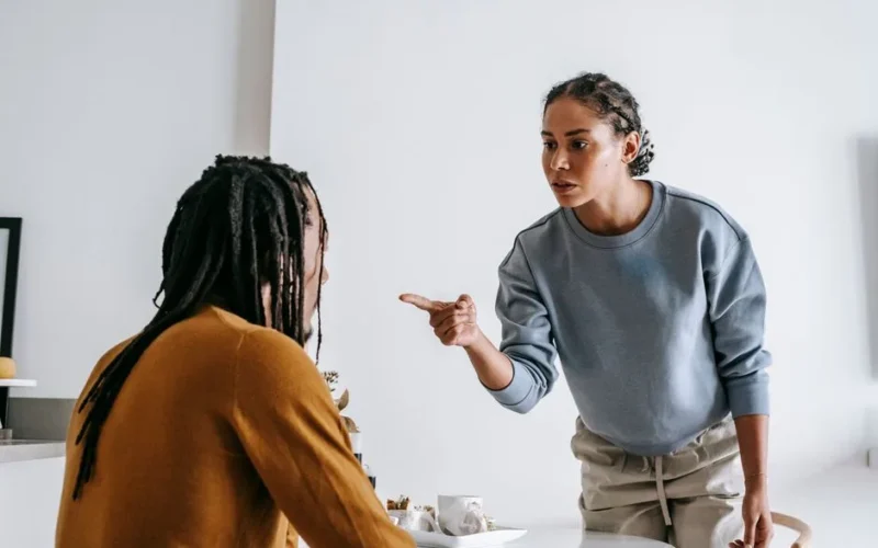 Young African American female standing near table while male sitting at kitchen and having argument