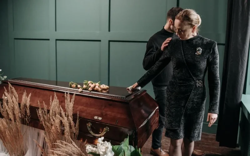 A solemn moment at a funeral with family mourning beside a coffin indoors.