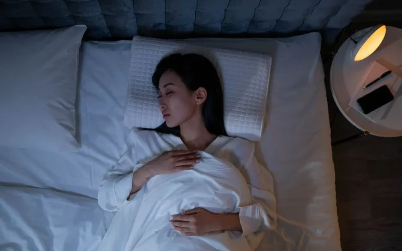 Calm and peaceful woman resting in bed under dim lighting, promoting relaxation.