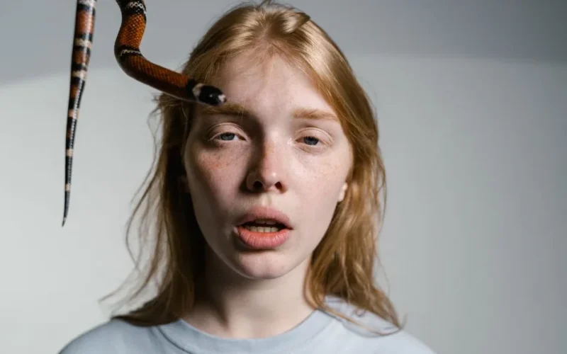 A woman shows fear as a snake approaches her face, depicting ophidiophobia.
