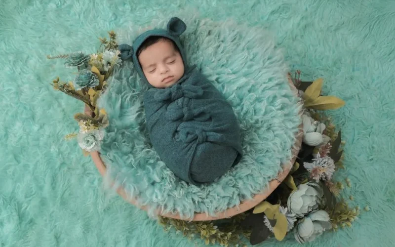A peaceful newborn baby wrapped in a teal blanket, surrounded by soft floral decor, capturing serene innocence.