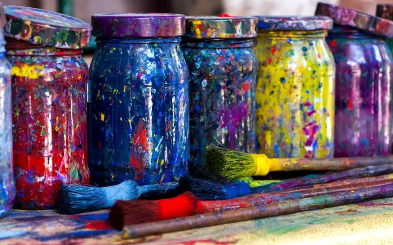 Vibrant mason jars splattered with paint alongside brushes in an Istanbul art studio.