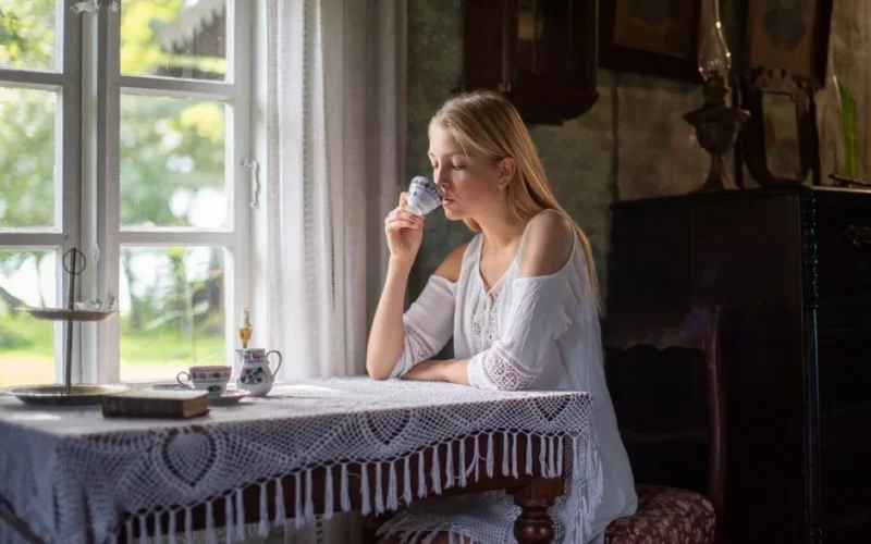 A serene moment of sipping tea by the window in a rustic Estonian cottage