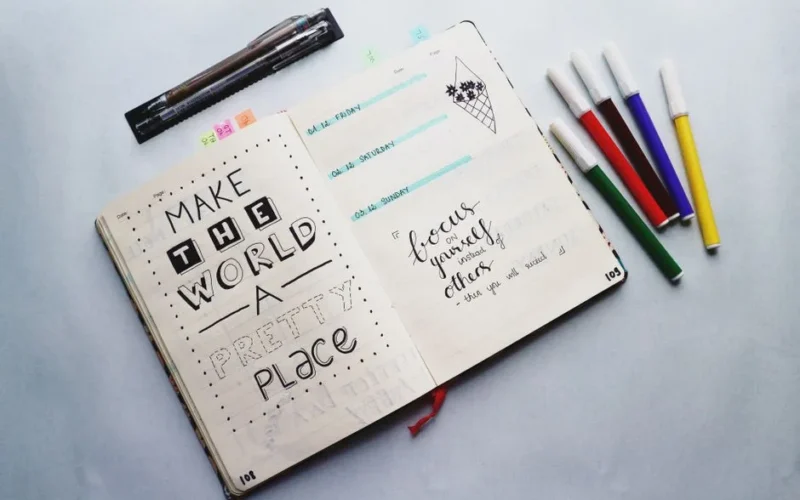 Open bullet journal with quotes and colorful markers for planning and creativity.