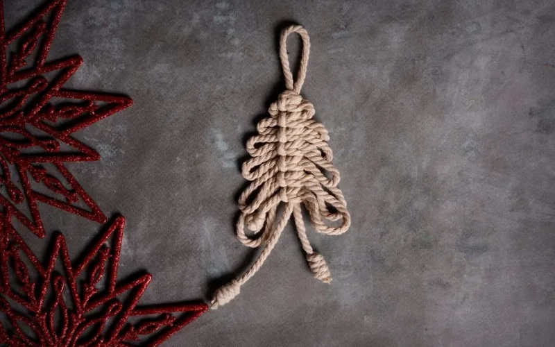 Artistic handmade rope Christmas tree with red decorations laid on a gray surface, perfect for holiday themes.