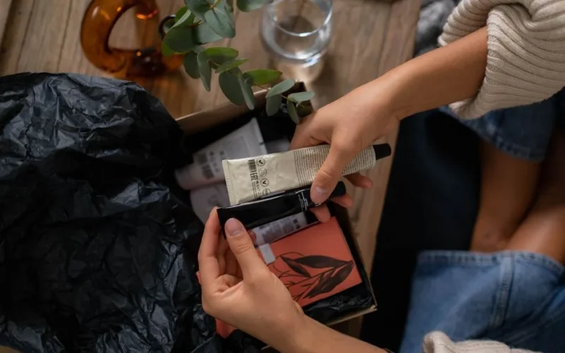 Hands unboxing skincare products with eucalyptus on wooden surface.