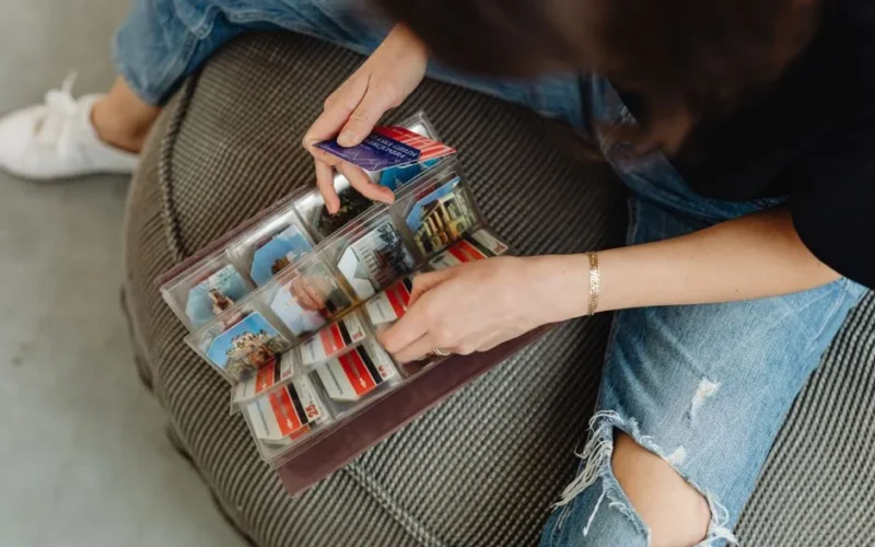 A person flipping through a photo album filled with travel souvenirs, sitting on a comfy chair.