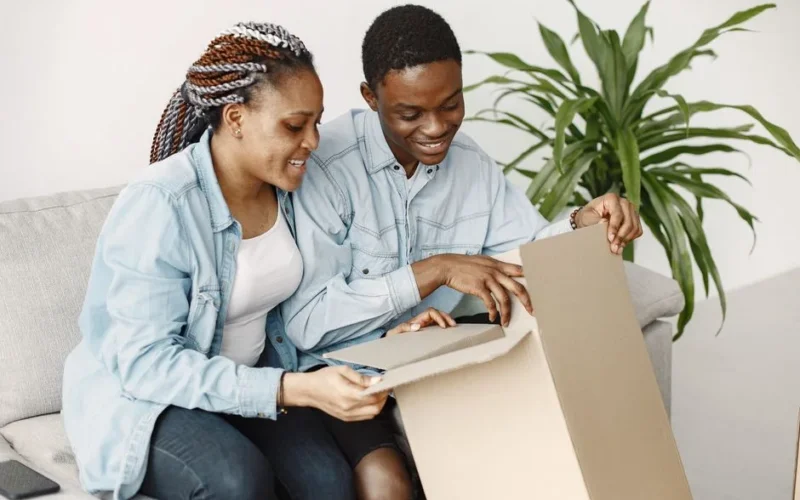Joyful couple opening a package together, seated on a living room sofa.