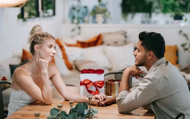 A loving couple enjoying a romantic date, holding hands indoors with a gift on the table.