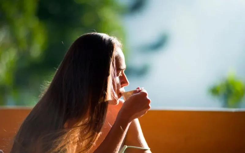 A woman peacefully sipping tea outdoors in the morning sunlight.