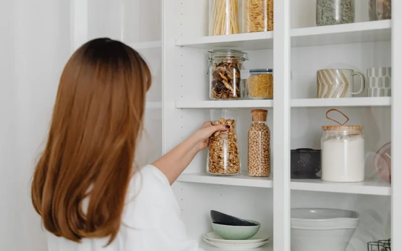 Woman arranging jars on pantry shelves for organized food storage.