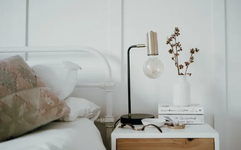 Stylish minimalist bedroom with a modern bedside table featuring a lamp, books, and decorative elements.