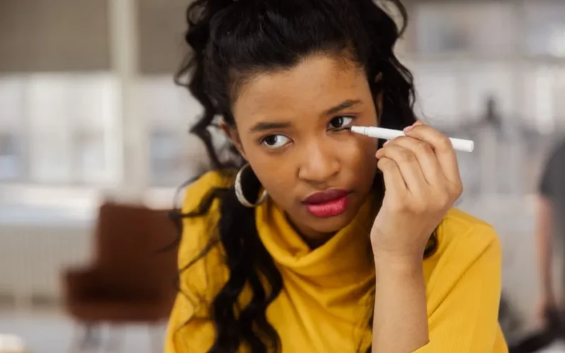 A focused young woman applying eyeliner in a well-lit indoor space.