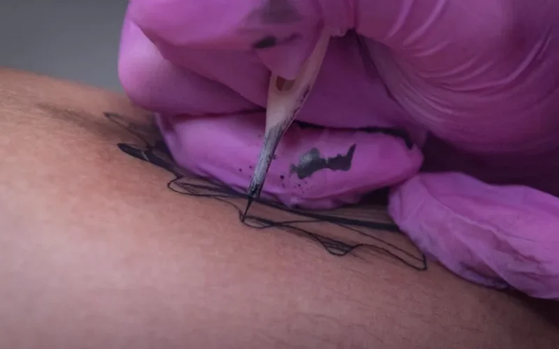 Close-up view of a tattoo artist inking a design on human skin.