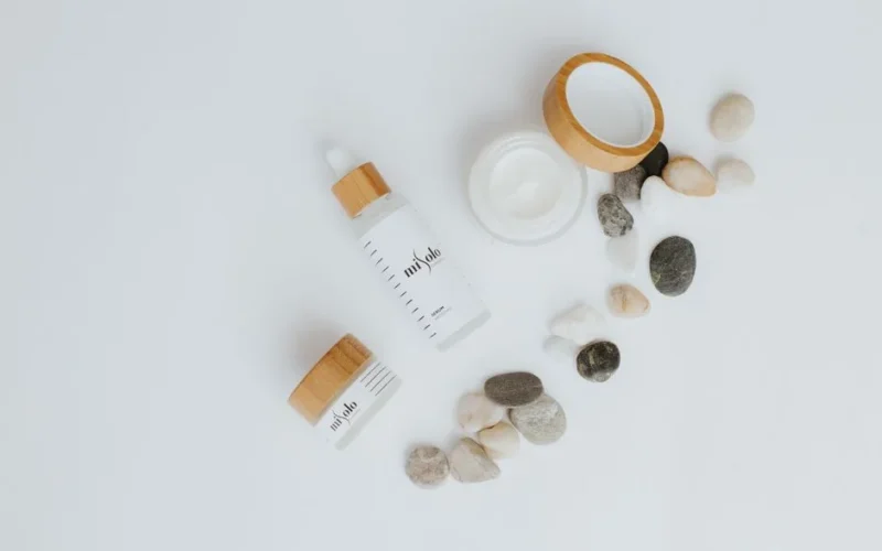 A flat lay of skincare bottles and jars with stones on a white background.