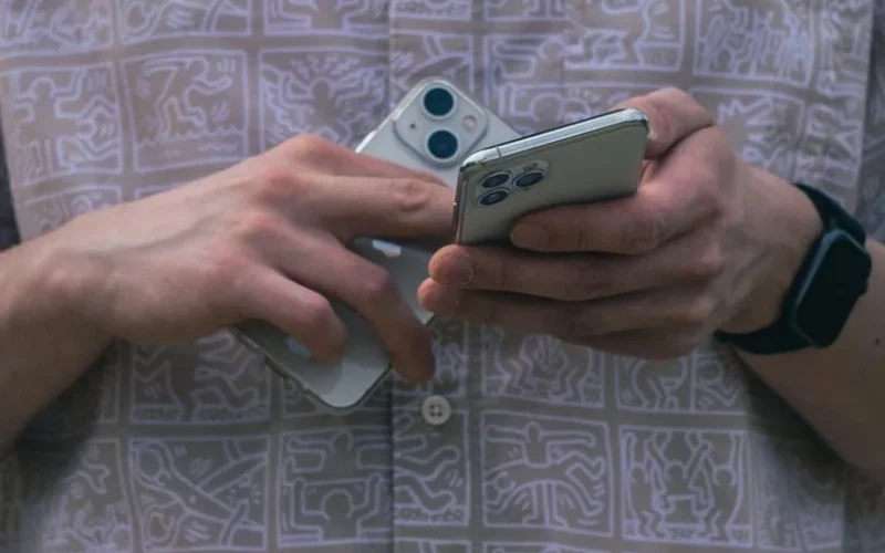 Detail of hands holding two smartphones, showcasing modern technology usage.