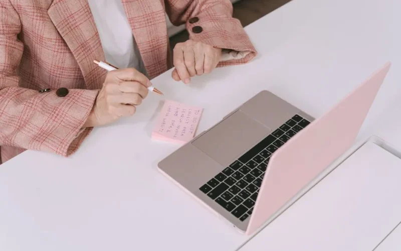 Businesswoman in a plaid jacket using a laptop and sticky notes for work planning.