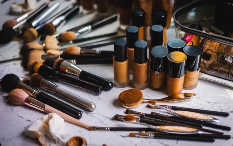 A variety of makeup brushes and foundation bottles arranged on a marble surface, showcasing beauty essentials.