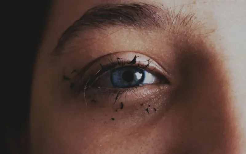 Detailed close-up of a blue eye with smeared mascara, capturing raw emotion.