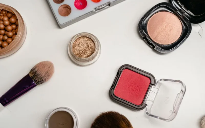 Flat lay of various makeup products including brushes, powders, and creams on a white surface.