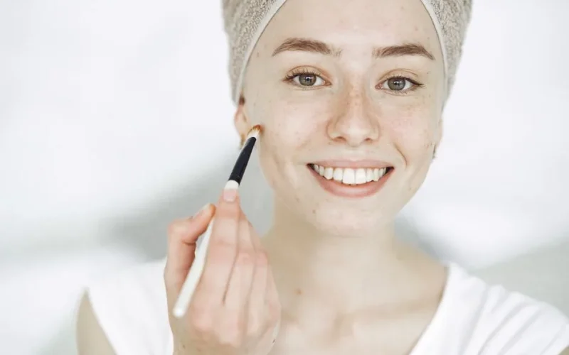 Close-up of a smiling woman applying makeup with a brush, enhancing natural beauty.