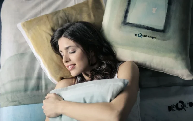 Woman peacefully sleeping in bed, hugging a pillow with a contented smile.