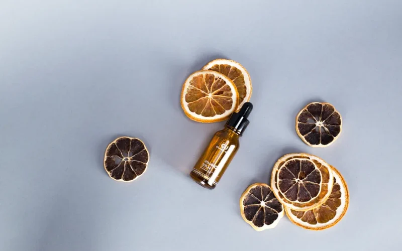 Flat lay of citrus slices and cosmetic serum bottle on gray background. Perfect for skincare and beauty themes.
