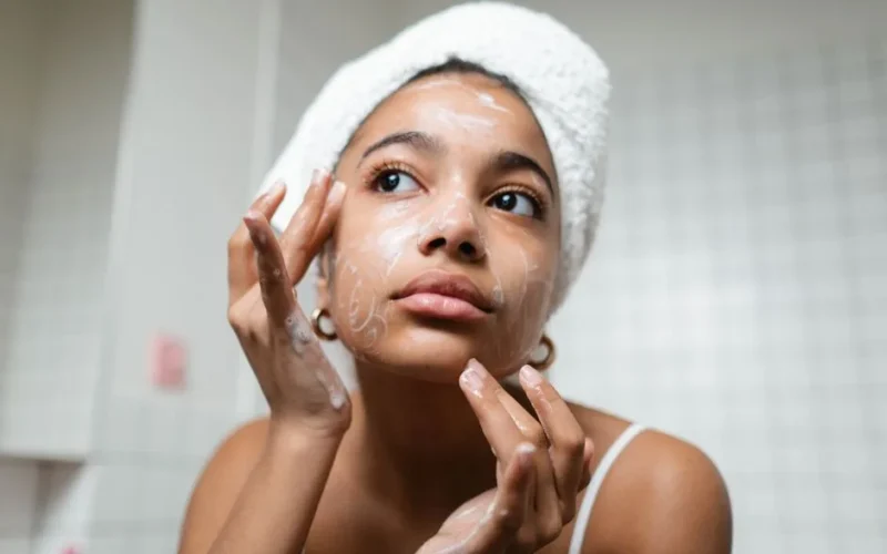 A young woman applies skincare cream in a modern bathroom setting.