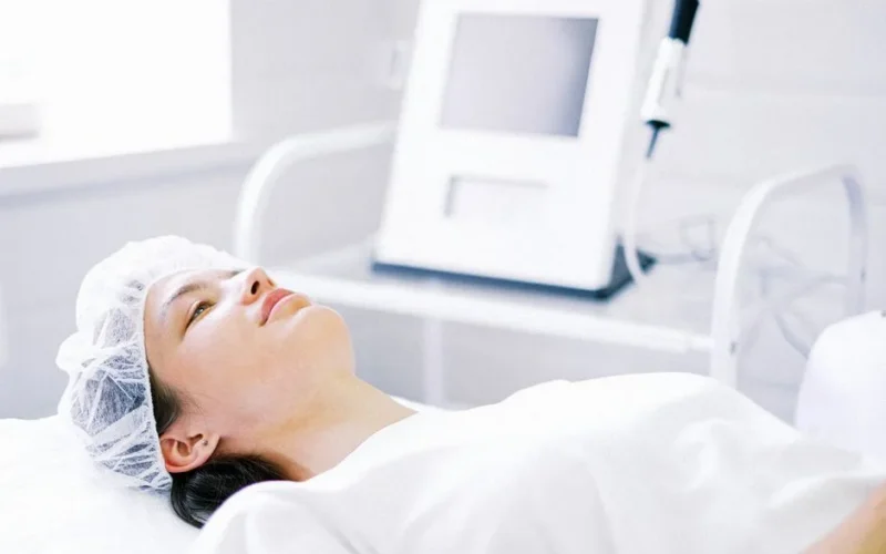 A young woman lying down for a beauty treatment in a clinic setting. She wears a hairnet.