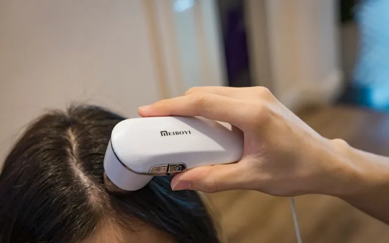 Close-up of a handheld device examining a person's scalp indoors.