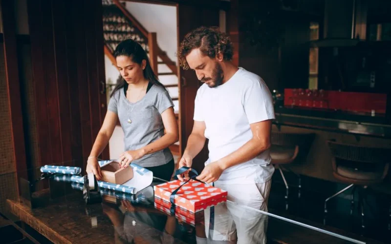 A couple wrapping gifts at a home dining table, creating a festive atmosphere.