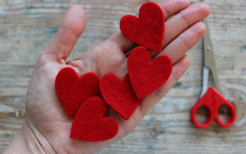 A hand holding red felt heart cut-outs on a wooden surface, ideal for Valentine's crafts.