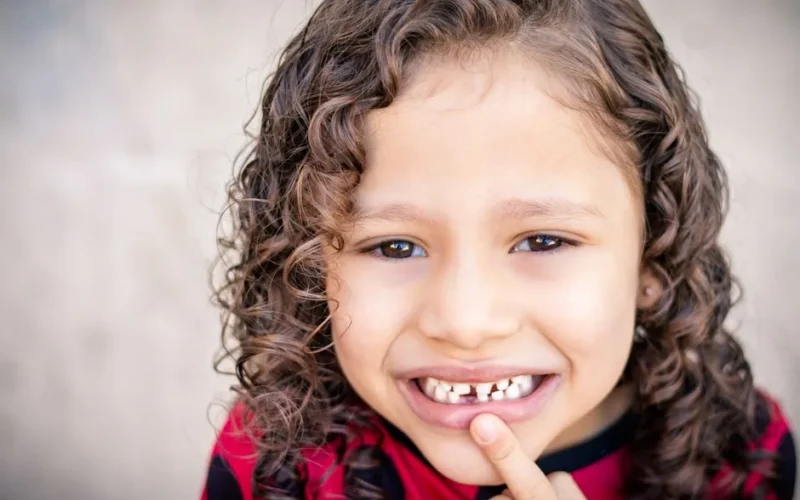 Close-up of a smiling child with curly hair showing a missing tooth, conveying happiness.