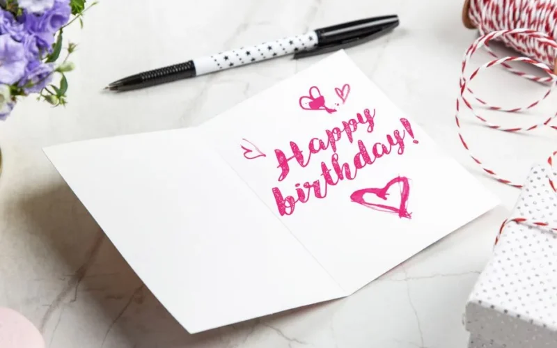 A vibrant birthday card with heart illustrations, surrounded by a pen, flowers, and gift wrap.