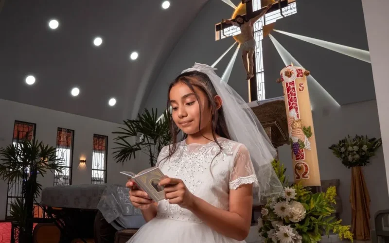 Young girl in white dress reading during communion ceremony in church.