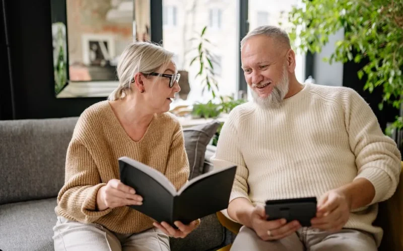 Smiling elderly couple reading and relaxing on a cozy sofa indoors.