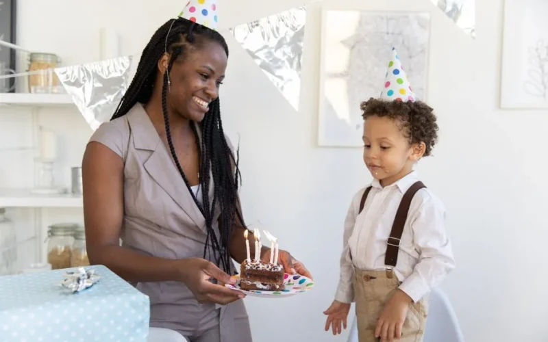 A woman and boy celebrate a birthday with cake and party hats indoors.