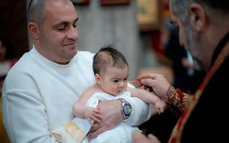 A father holds his baby during a religious baptism ceremony in a church setting.