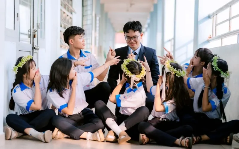 Group of happy students in uniform celebrating with their teacher in a hallway.