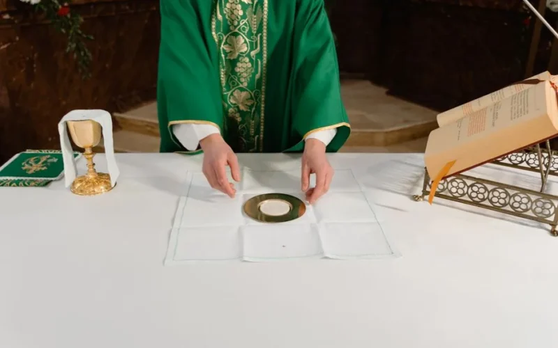 A priest in green vestments prepares the sacramental bread during a Catholic mass ceremony.