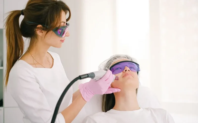 A cosmetologist performing laser treatment on a woman in a clinic setting.