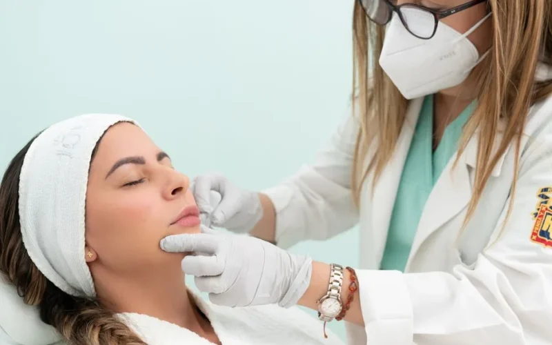 Doctor performing cosmetic treatment on a woman with eyes closed in a clinical setting.