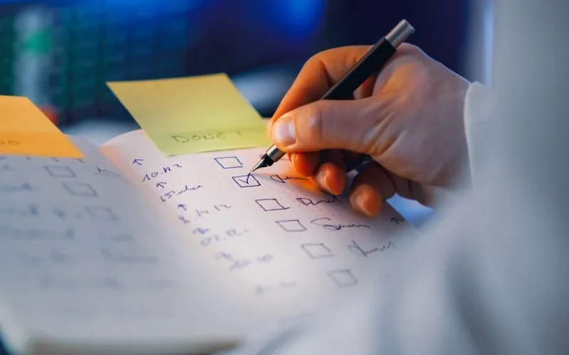 Close-up of a hand writing in a notebook with checkboxes, highlighting productivity and organization.
